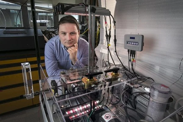 A man in a blue shirt stands behind cannabis grow lights and equipment in a lab, showcasing cannabis lighting technology.