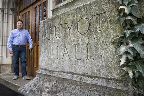 A man stands by Guyot Hall with stone sign, highlighting cannabis lighting technology.