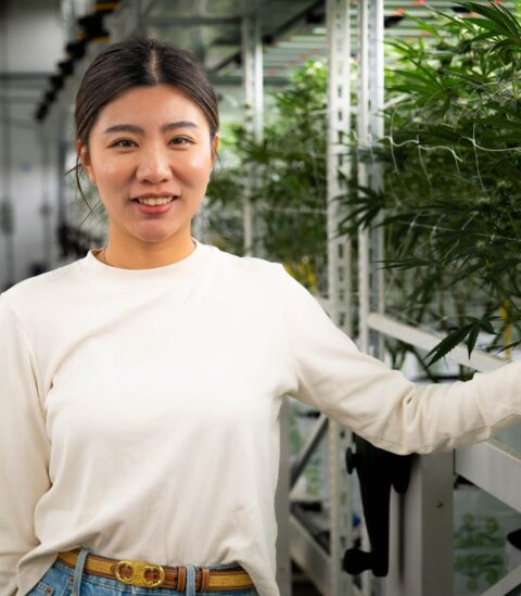 Smiling person in greenhouse touching LED lighting structure by Fluence; vibrant green plants in background, Austin-based controlled environment agriculture lighting experts specializing in crop yield optimization including cannabis.