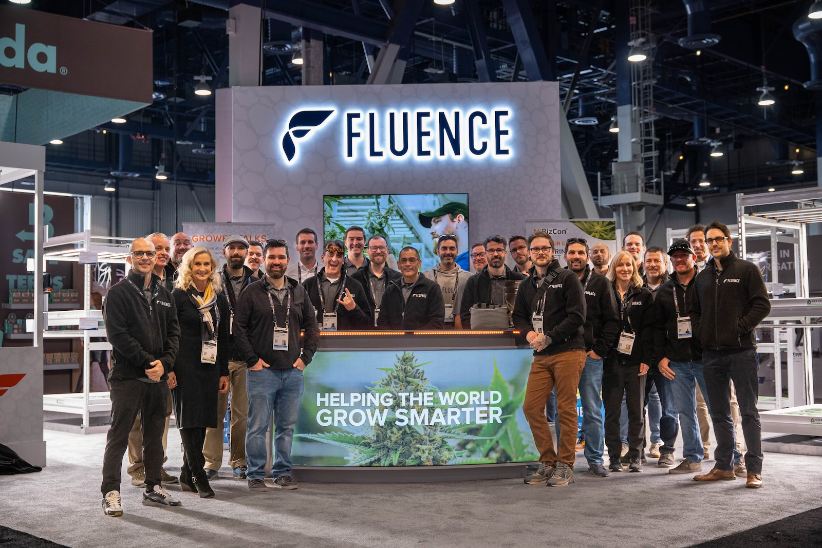 A group of individuals stands in front of the Fluence booth, showcasing advanced LED lighting for controlled environment agriculture, promoting smarter crop production including cannabis cultivation, Austin, Texas-based.