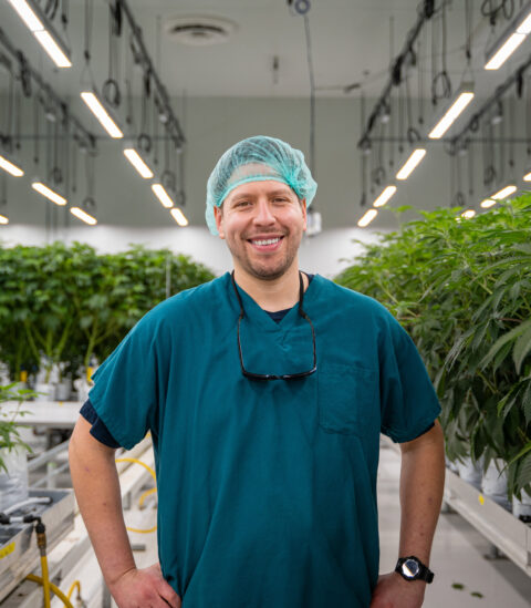 A person in scrubs and hairnet smiling in cannabis cultivation greenhouse showcasing Fluence LED lighting solutions for optimized crop production.