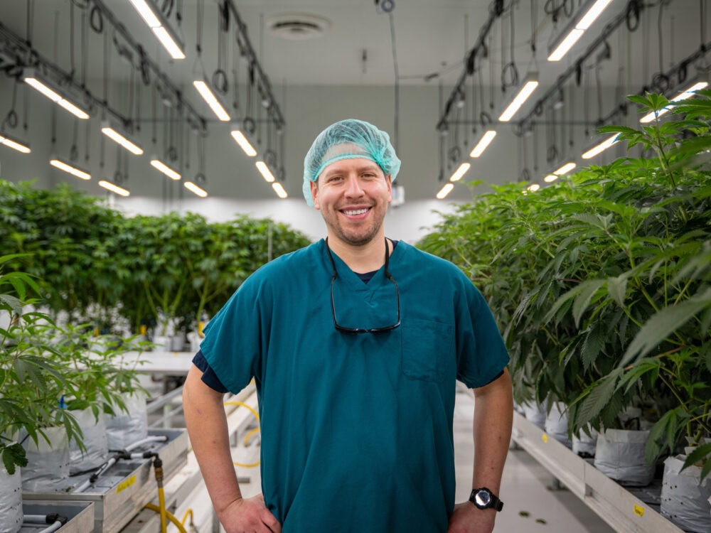 A person in scrubs and hairnet smiling in cannabis cultivation greenhouse showcasing Fluence LED lighting solutions for optimized crop production.