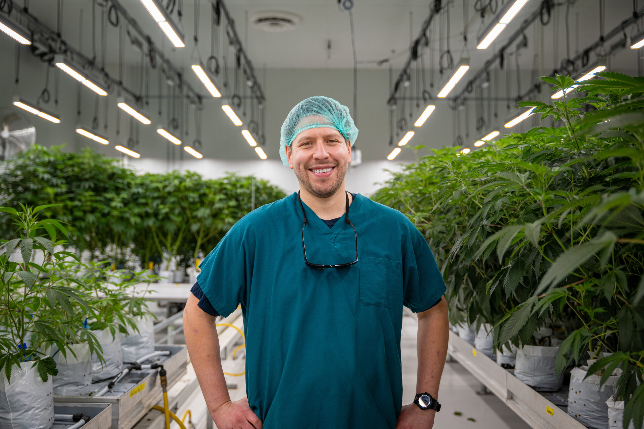 A person in scrubs and hairnet smiling in cannabis cultivation greenhouse showcasing Fluence LED lighting solutions for optimized crop production.