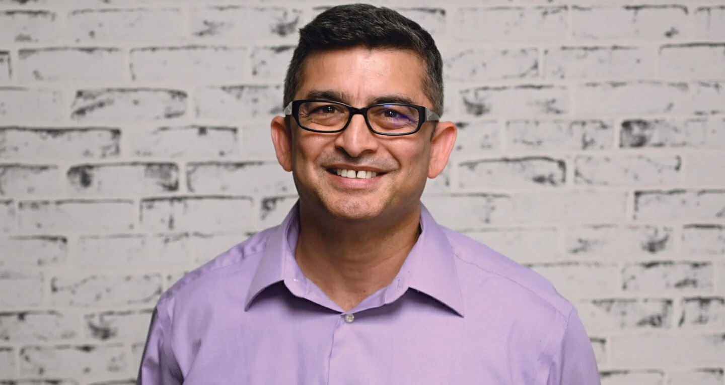 Smiling man in glasses and purple shirt with cannabis LED grow lights display.