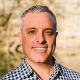 Smiling gray-haired man in checkered shirt outdoors, representing Fluence, an Austin-based LED lighting company specializing in optimized crop production and cannabis cultivation.