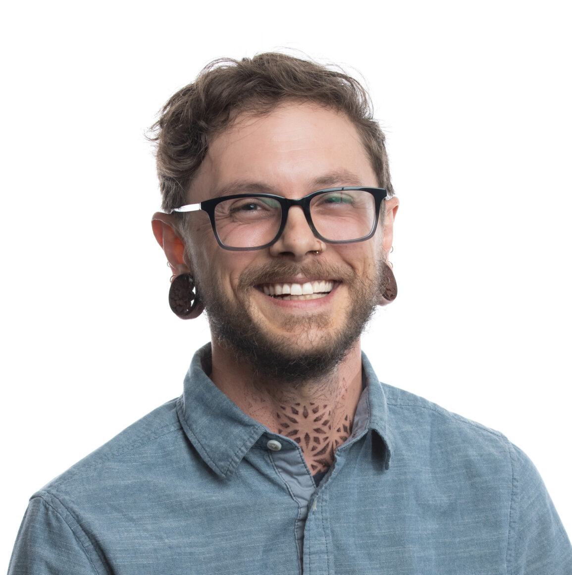 Portrait of a smiling person with glasses and facial piercings, dressed in a blue button-up shirt; representative of Fluence, Austin's leading LED lighting innovator for controlled environment agriculture and cannabis cultivation.