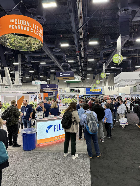 Fluence LED lighting solutions booth at Austin expo, showcasing advanced cannabis cultivation lights for optimized crop production. Attendees explore various LED lighting setups in a crowded hall with hanging signs above.