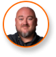 A bearded man in a dark shirt smiles, framed by an orange circle; cannabis grow lights expert.