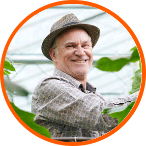 Un hombre mayor con sombrero de paja entre plantas de cannabis bajo luces LED de cultivo.